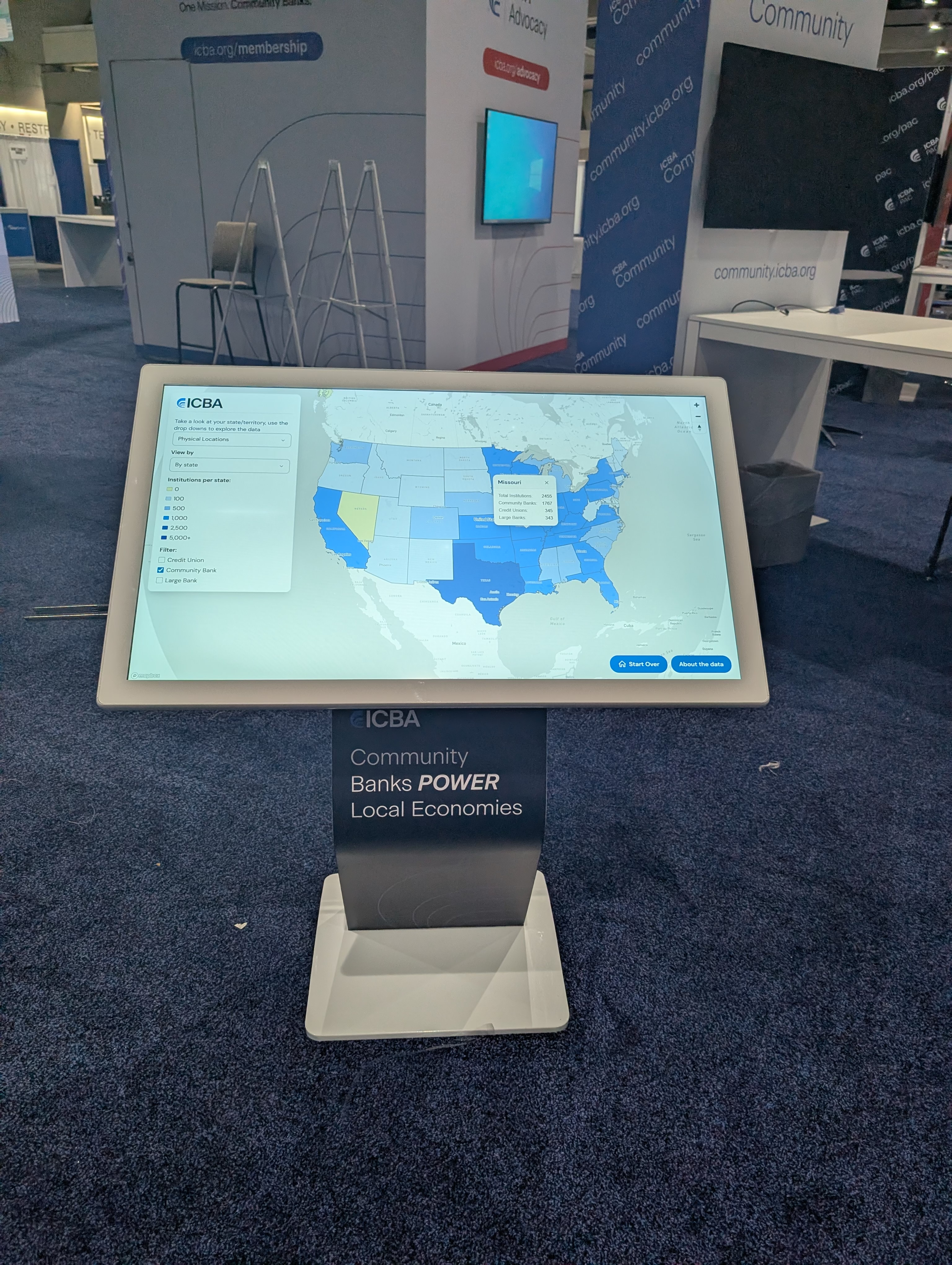 Large-format touch table displaying an interactive state-by-state map of community bank lending on a trade show floor.